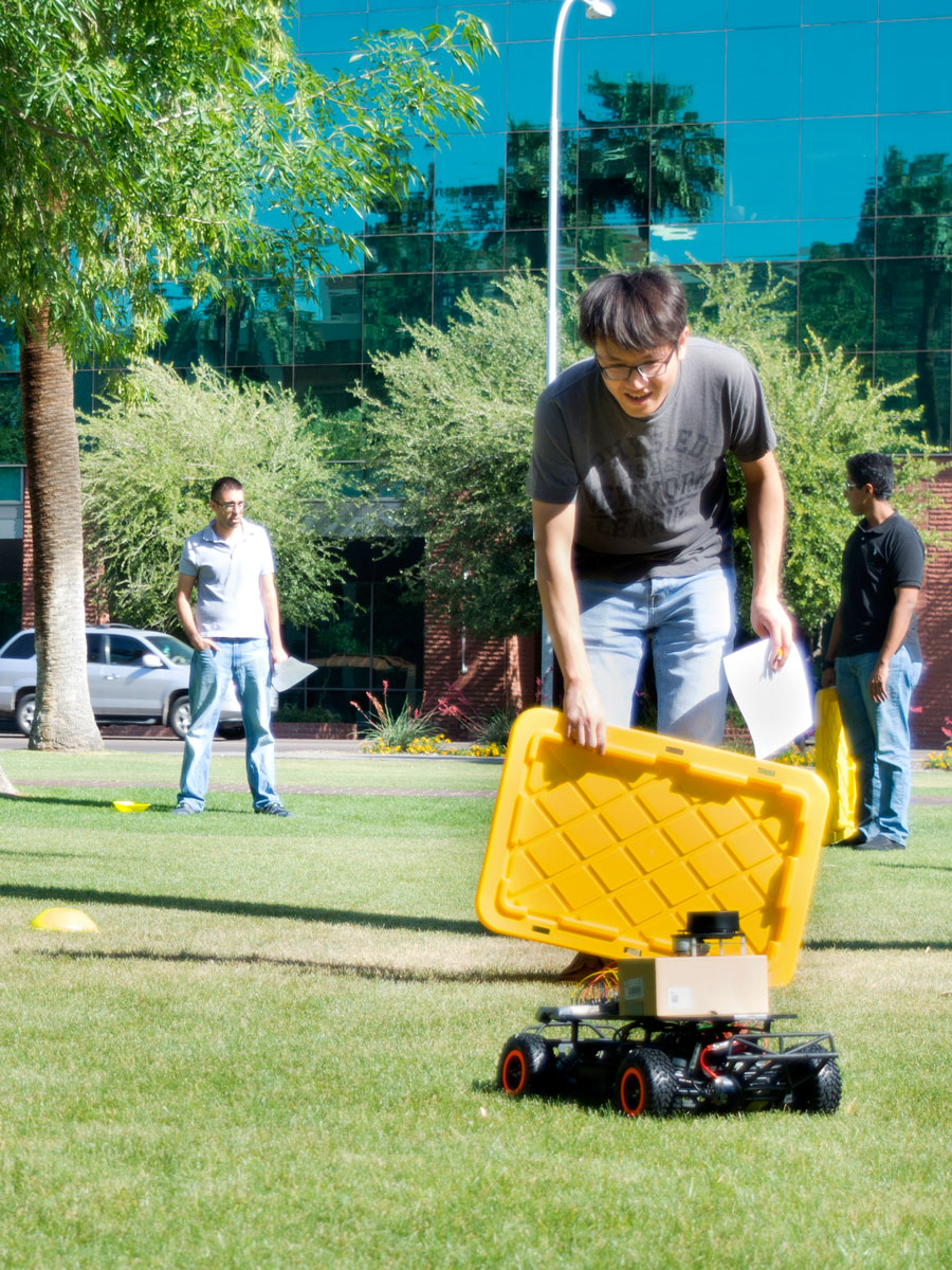 A student holds up a crate lid to test his car's ability to sense an obstacle in its path.