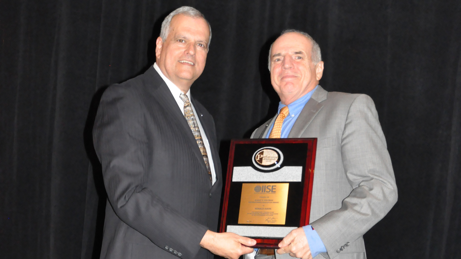 Photo of two men holding a plaque. Caption says "Professor Ron Askin, former director of the School of Computing, Informatics, and Decisions Systems Engineering, accepts the Albert G. Holzman Distinguished Educator Award from Tim McGlothlin, Institute of Industrial and Systems Engineers 2017-18 President-Elect, at the IISE annual awards gala, held May 22 in Pittsburgh. Photo courtesy of IISE"