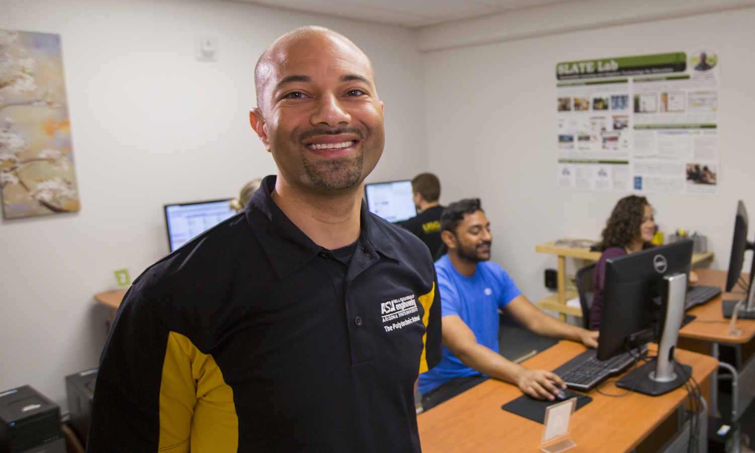Portrait of Rod Roscoe in a computer lab. Caption "Rod Roscoe, assistant professor of human systems engineering, works with students in his SLATE Lab to improve engineering education. His efforts led to a prestigious Tooker Professorship to advance his work in developing an engaging human systems engineering curriculum at Arizona State University's Ira A. Fulton Schools of Engineering. Photographer: Jessica Hochreiter/ASU"