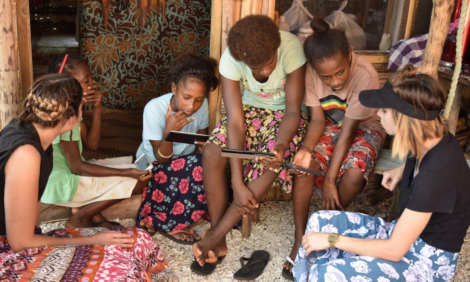 Photo of two female ASU students showing educational content to local girls on island of Nguna. Caption: On the island of Nguna, a community that lacks access to electricity, internet and running water, Brittany Blevins (far left) and Brianna Fornes (far right) show some of the local children the educational content available on the SolarSPELL