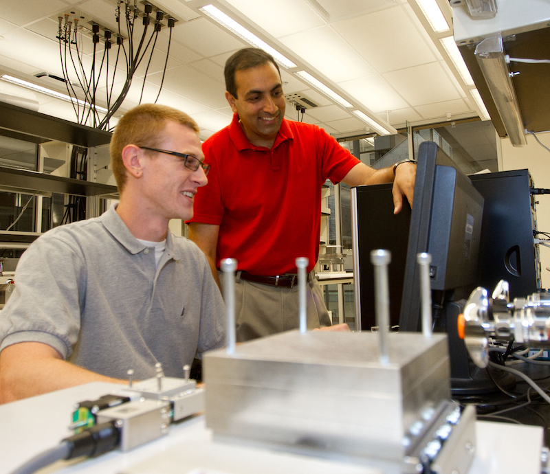 Photo of Nik Chawla pointing at a monitor while a student sits next to him. 