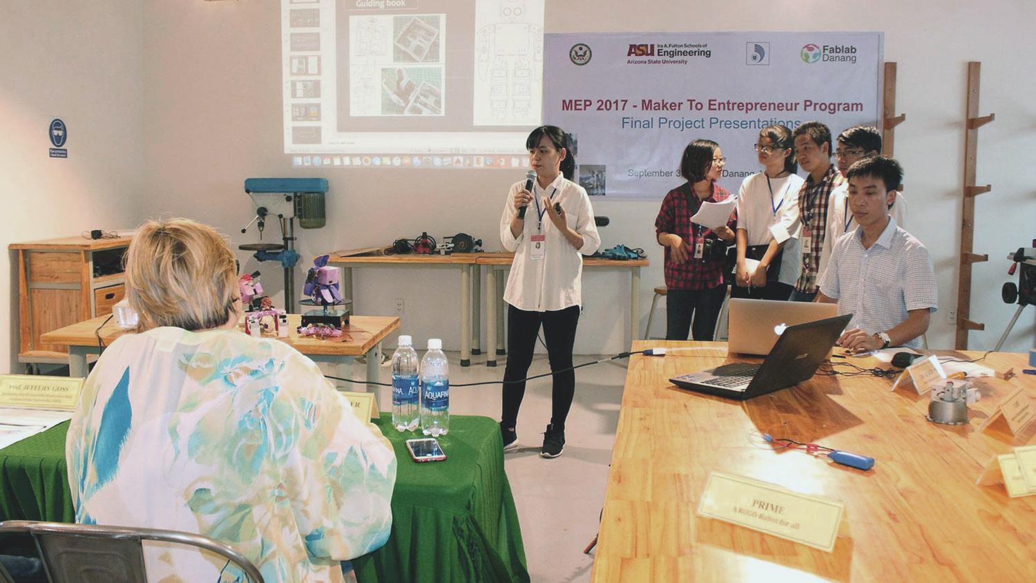 Photo of female speaking as part of a group in front of a room. Caption: Vietnamese student teams presented product prototypes at the Maker to Entrepreneur Program’s competition at University of Danang’s Maker Innovation Space in September 2017. Photo courtesy of Thao Nguyen