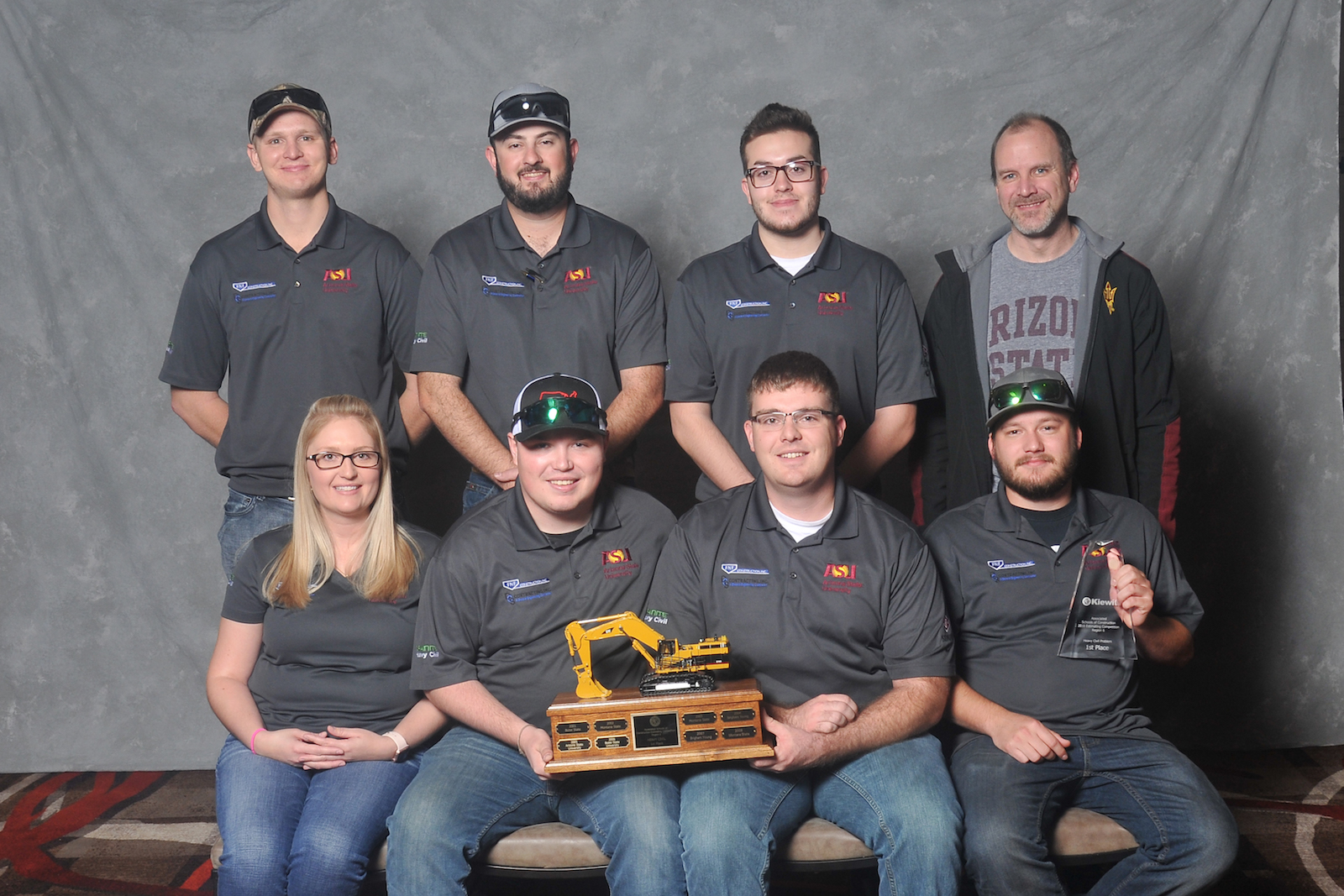 Photo of eight people posed holding a trophy. Caption: First-place heavy/civil team: (left to right, back to front) Jacob Dittbrenner, Samuel Schlinger, Nathan Eldodt, coach Aaron Cohen, Brittany Wells, Tanner Schafersman, Jacob Ellis and Shay Snider. Photo by Associated Schools of Construction for Regions 6 and 7