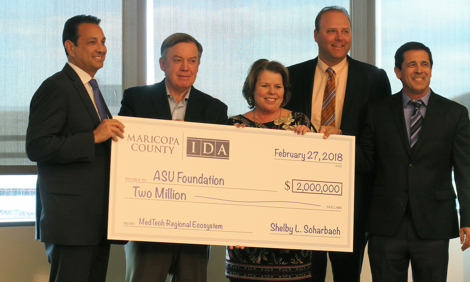Photo of five people standing behind an oversized check. Caption: ASU President Michael Crow (second from left) accepts $2 million check to kick off a medical technology workforce development initiation. Pictured with Maricopa County Board of Supervisors Chairman Steve Chucri, District 2, MCIDA Executive Director Shelby L. Scharbach, MCIDA Board Member Jeremy Stawiecki, and MCIDA Business Development Officer Gregg Ghelfi. Photographer: Charrie Larkin/ASU.