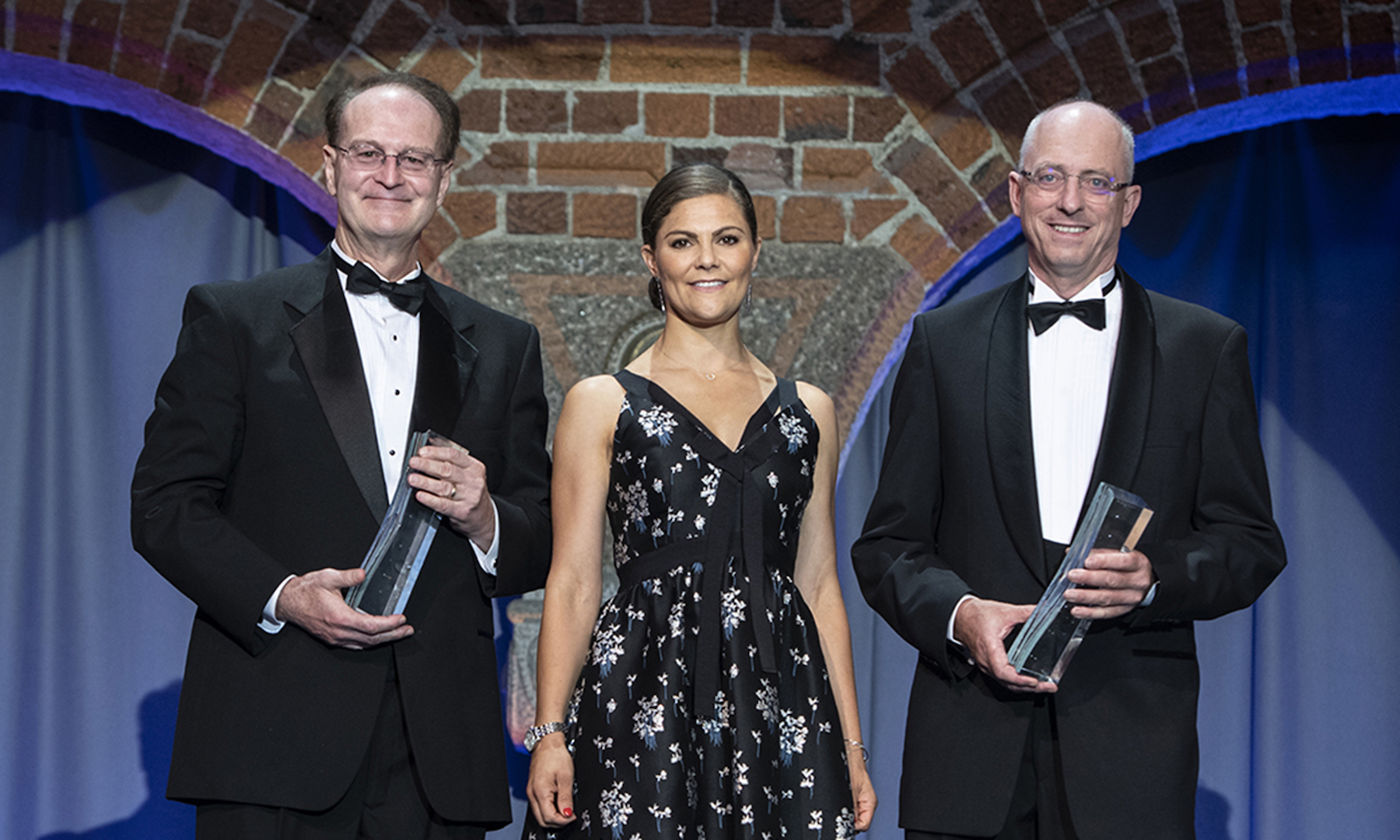 two men standing and holding awards with a woman in the middle