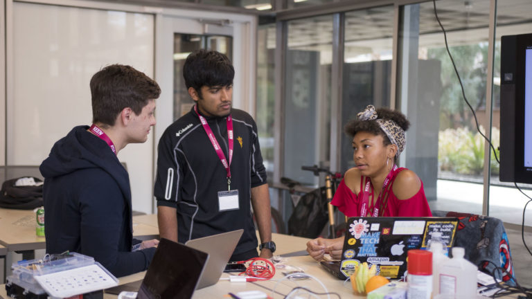 Photo of three students working at a table together. Caption: ASU students worked with students from around the globe during Devils Invent's – Invent for the Planet to solve high impact, global problems together. Photographer: Marco-Alexis Chaira/ASU