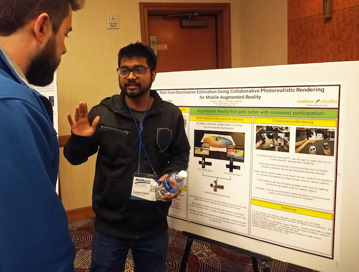Photo of student presenting in front of poster. Caption: Computer science graduate student Siddhant Prakash presents his poster highlighting research on environmental sensing for mobile augmented reality applications to a fellow ACM HotMobile ‘18 attendee. Prakash won Best Poster out of 16 posters at the workshop. Photo courtesy of Robert LiKamWa. 