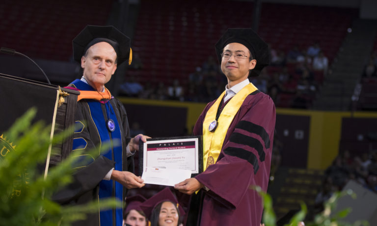 Photo of Steve Phillips and Zhengshan “Jason” Yu holding a plaque. Caption: Zhengshan “Jason” Yu receives the Palais Outstanding Doctoral Student Award from School of Electrical, Computer and Energy Engineering Director Steve Phillips at the Ira A. Fulton Schools of Engineering Spring 2018 Gold Convocation Ceremony at Wells Fargo Arena, May 9, 2018. Photographer: Marco-Alexis Chaira/ASU