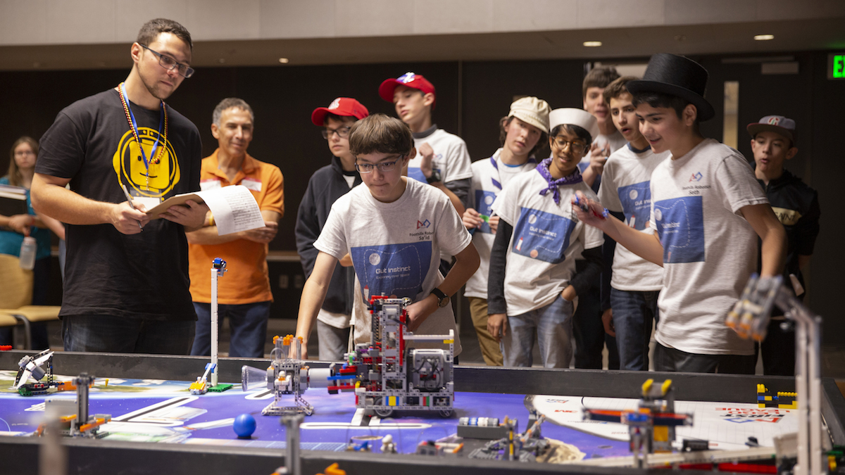 group of young students cheering on a robot