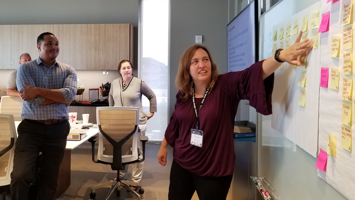 woman pointing at a white board covered in sticky notes