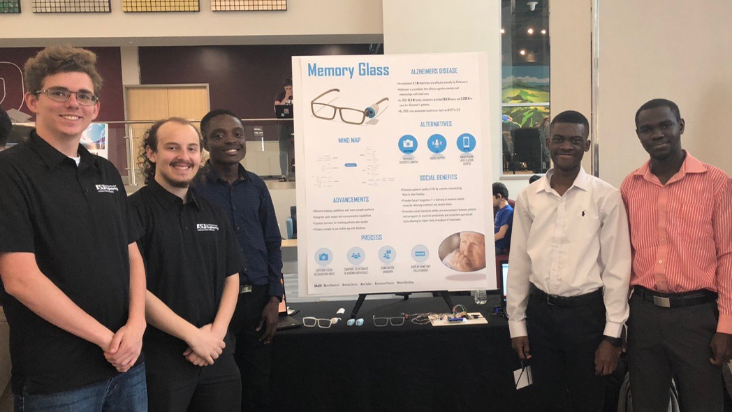 five students standing in front of a poster