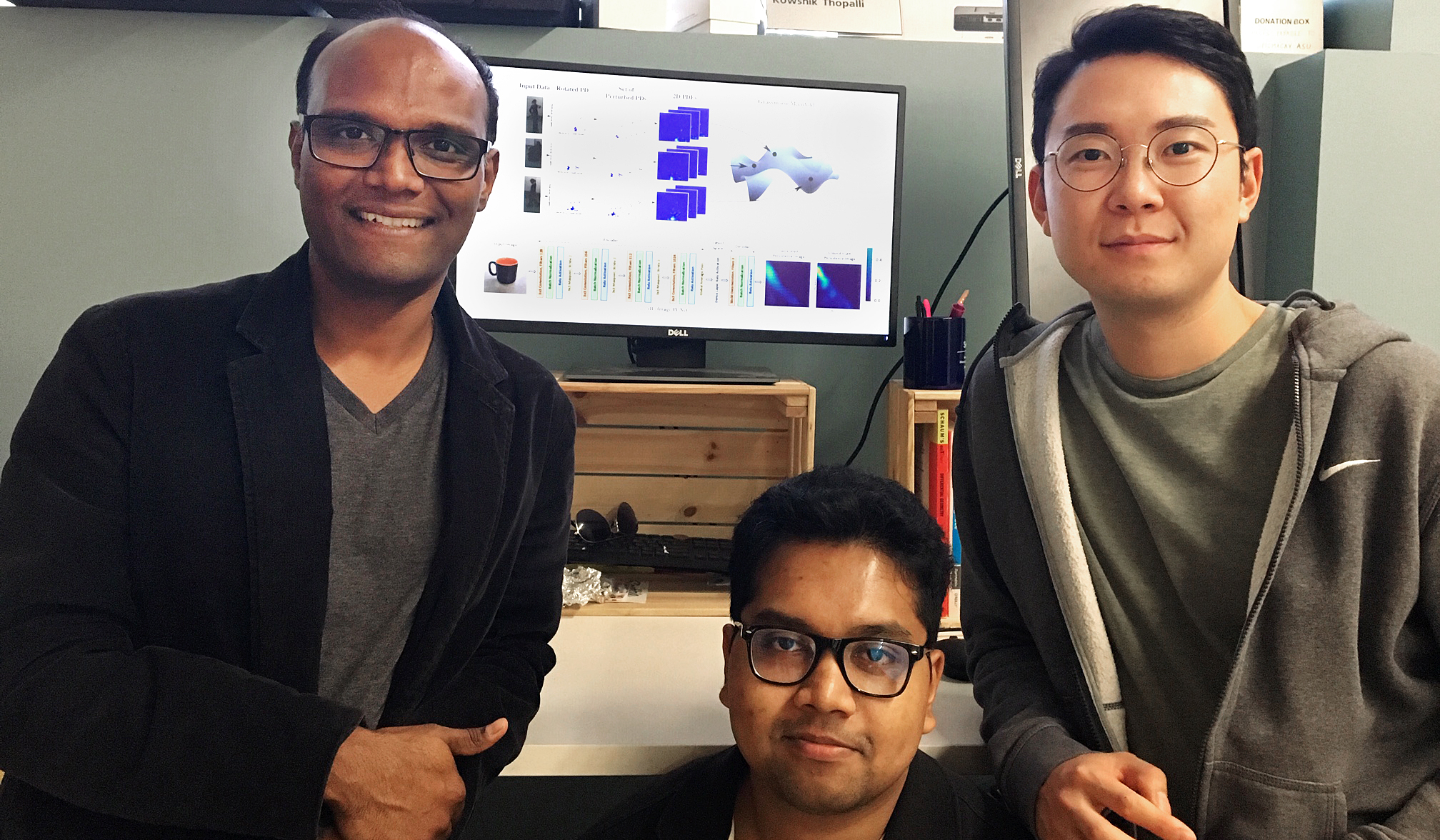 Three men posing in front of monitor