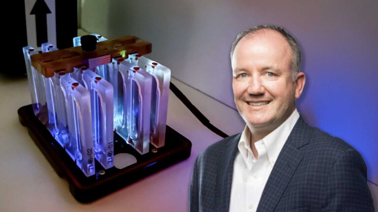 ASU Regents Professor Paul Westerhoff standing in front of experimental hardware for the Germicidal Ultraviolet Light Biofilm Inhibition (GULBI) investigation. The setup features four parallel reactors with glowing blue BioCells, illuminated by side-emitting optical fibers and LEDs.