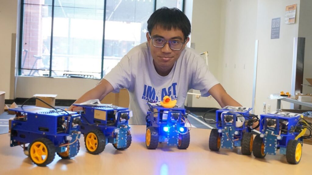 Khoa Vo poses with small, robotic vehicles.