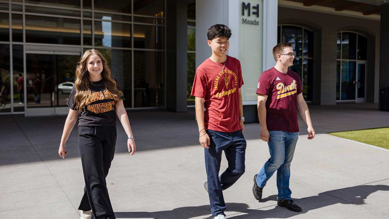 Three students dressed in ASU gear walk by the Meade building.
